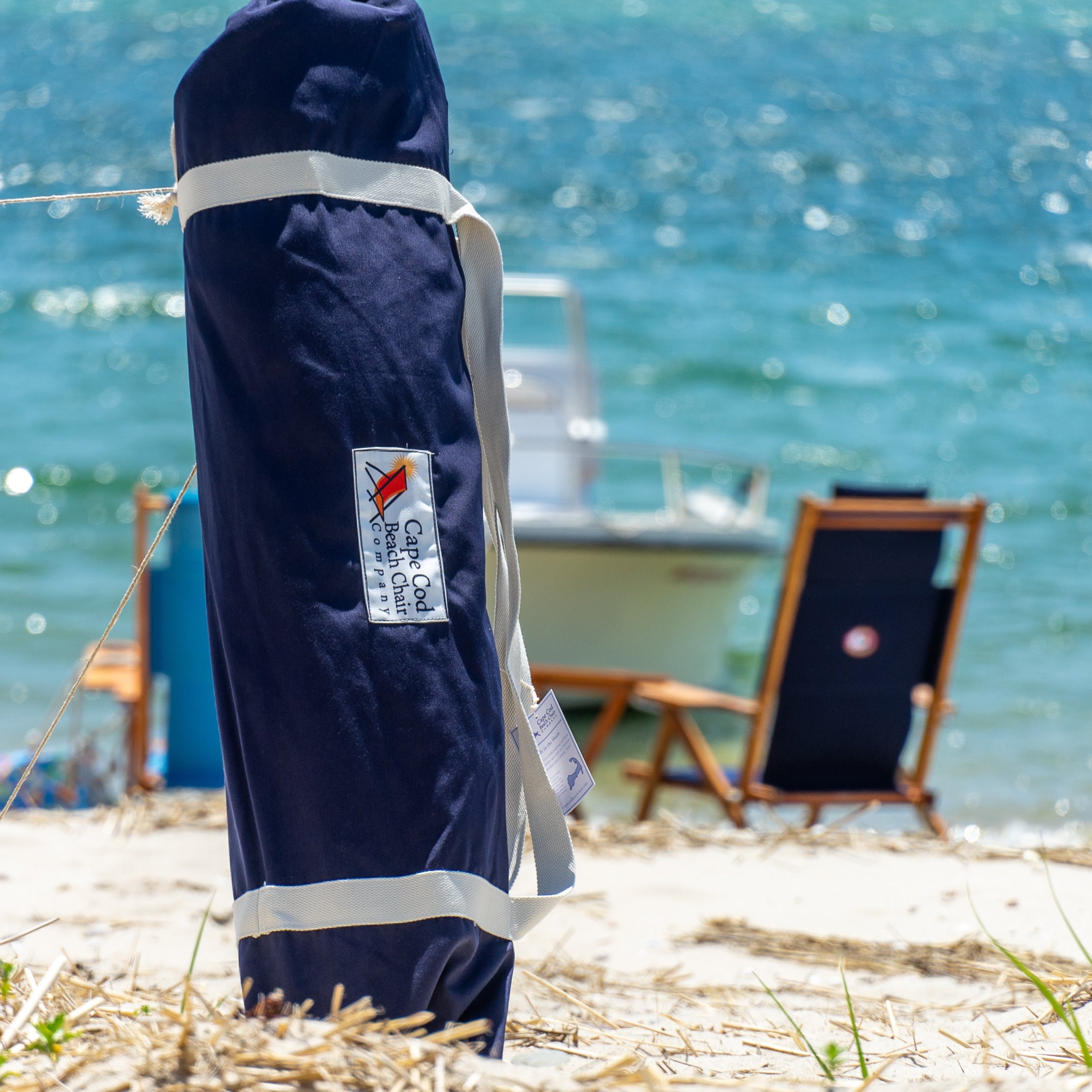 Navy umbrella in carrying bag on beach with wood beach chairs