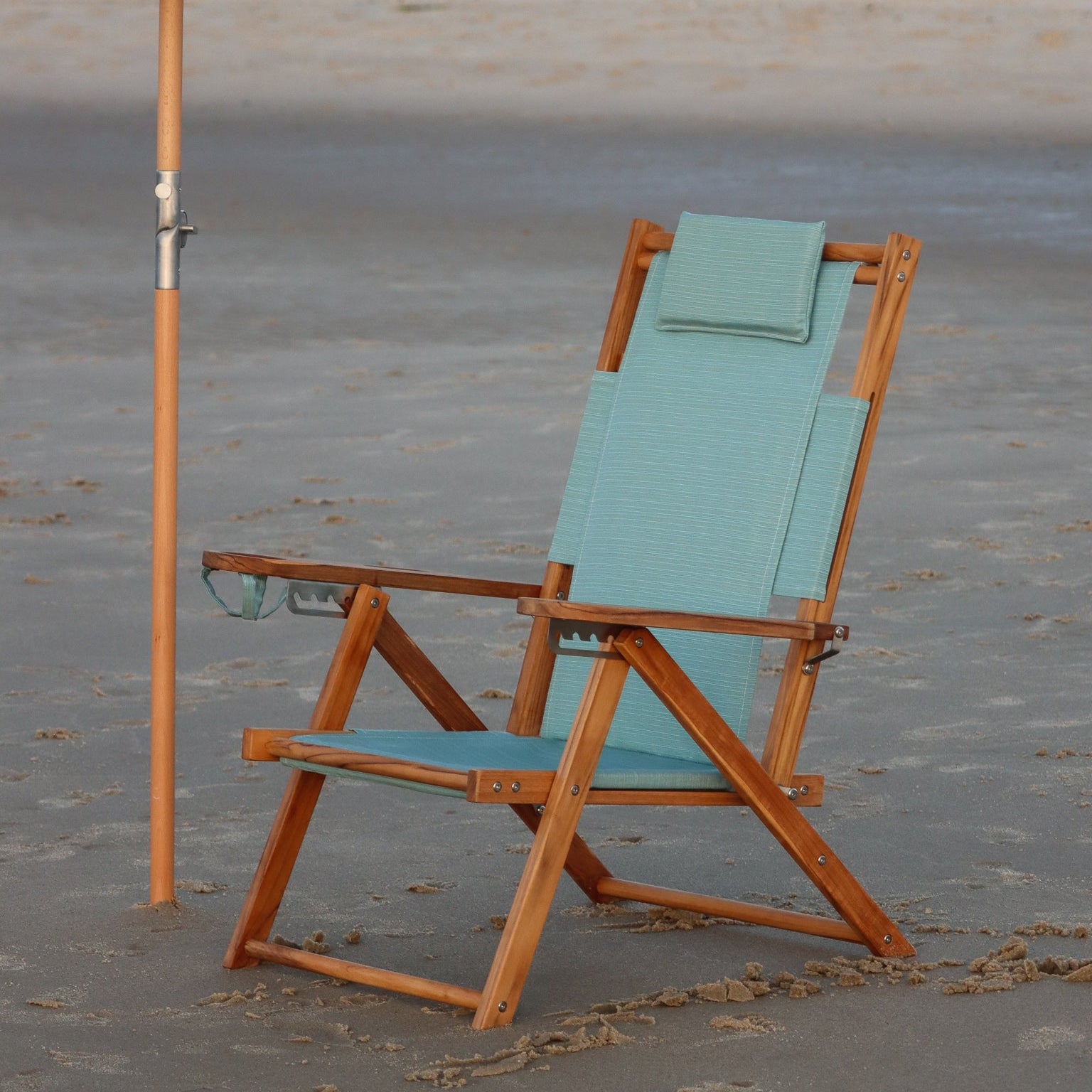 Beach chair with wooden frame and seafoam fabric on a sandy beach.