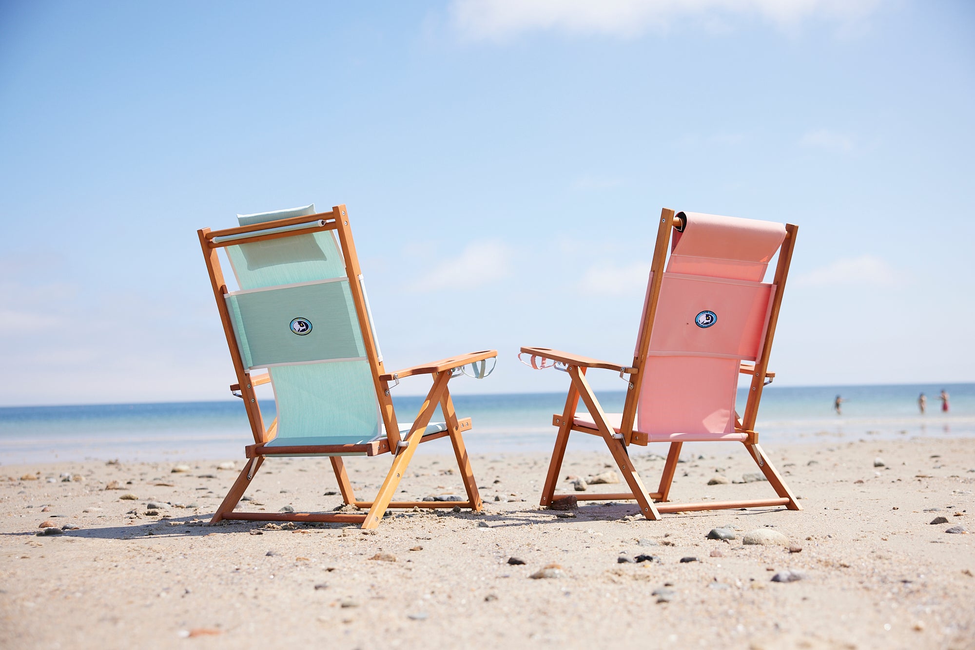 Two beach chairs, one seafoam and the other coral pink, on a beautiful beach.
