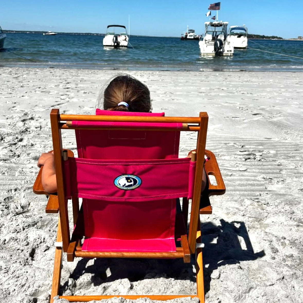 A girl sits in a pink beach chair on the beach in Plymouth MA.