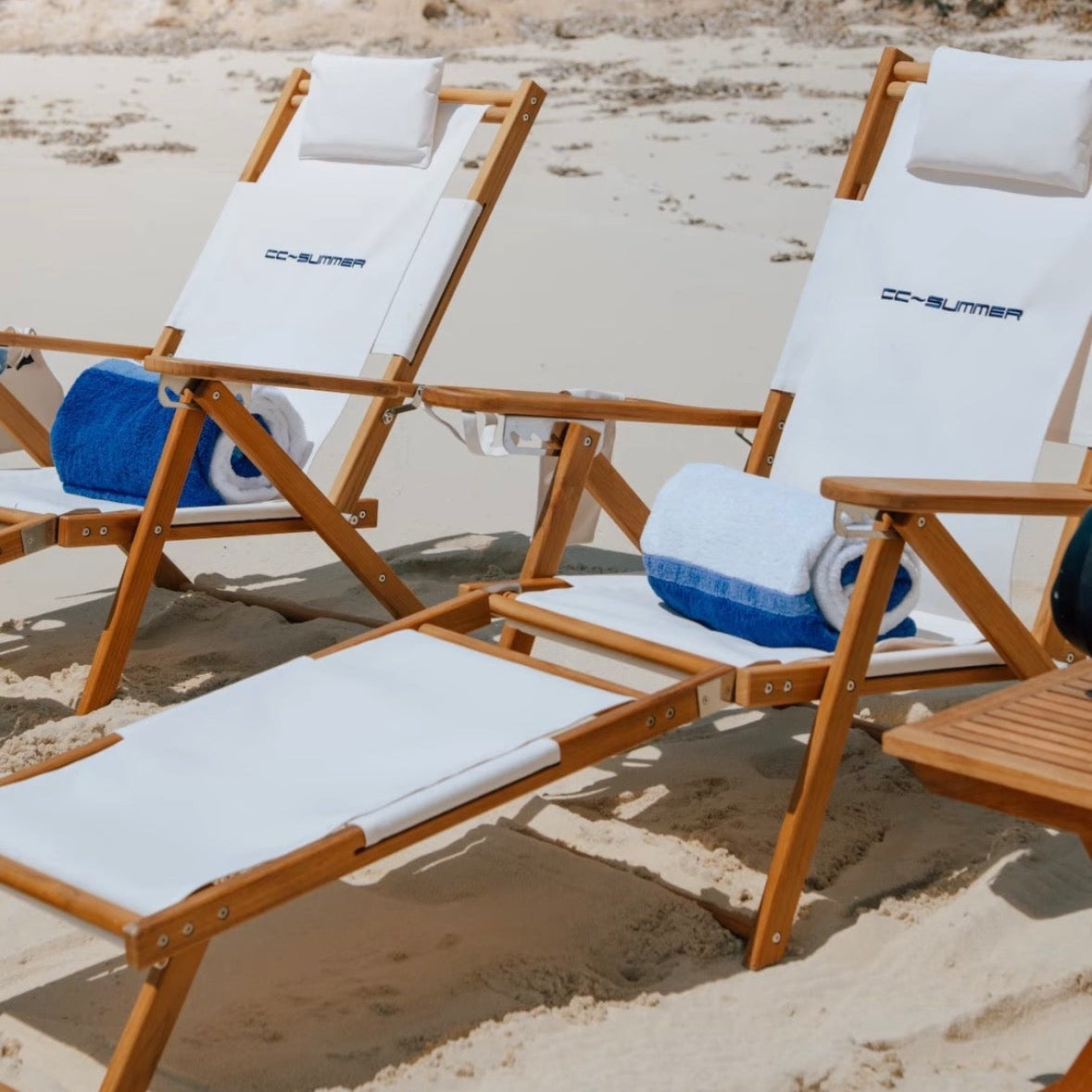A pair of white beach chairs made of teak, on a sandy beach in the Caribbean.