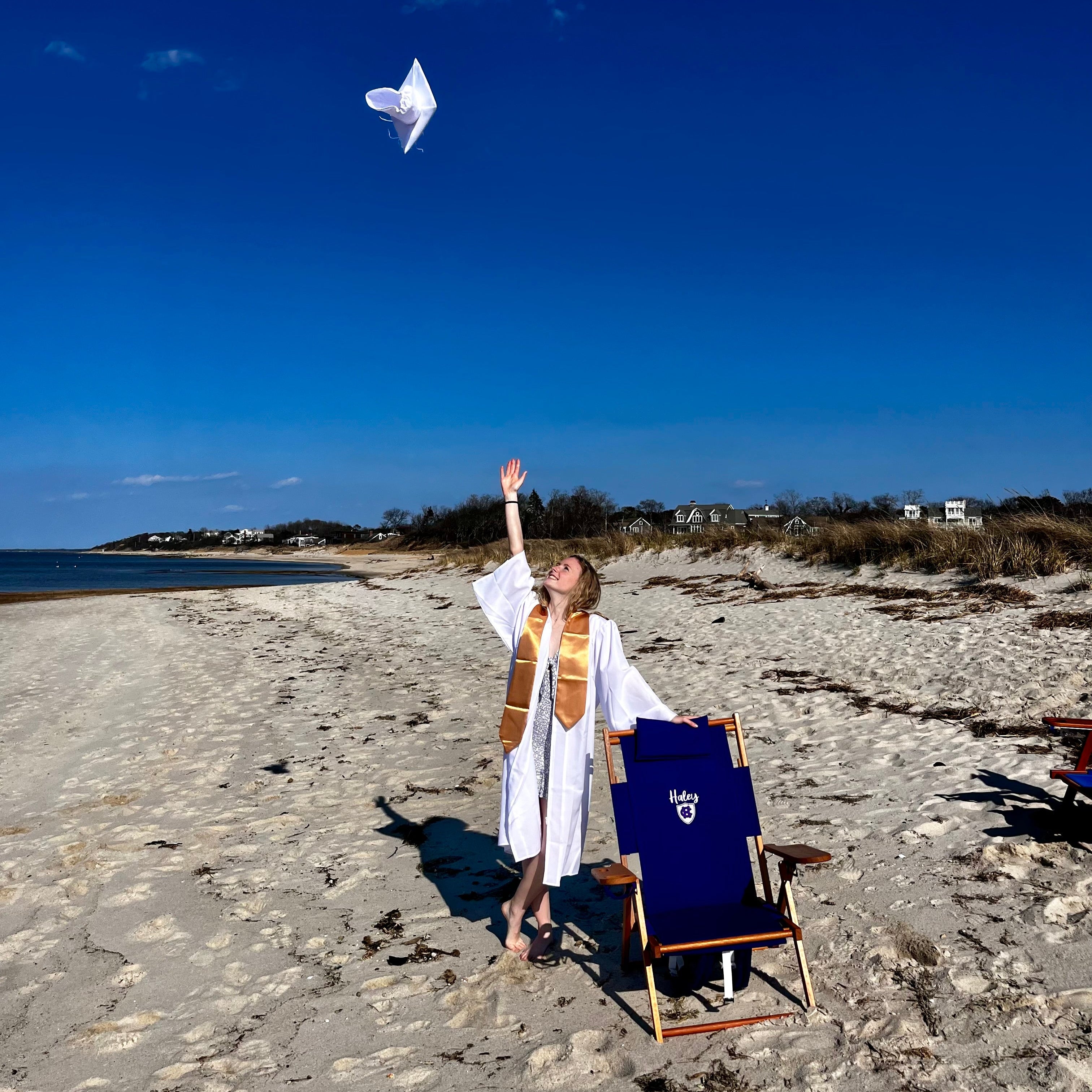 High School Graduate Throwing Cap on Beach with Custom Wood Holy Cross Beach Chair