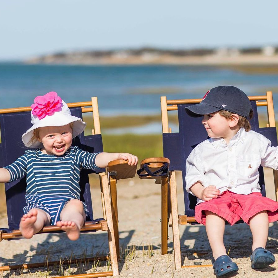Two children sitting on beach chairs by the ocean