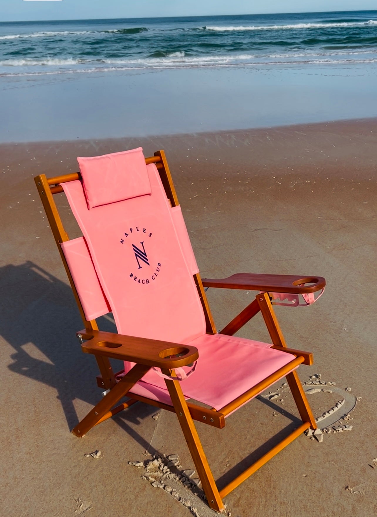 A luxury wood beach chair with flamingo pink fabric and custom embroidered logo at the Four Seasons Naples Beach Club in Naples, FL.