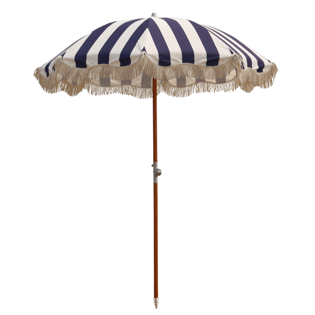 A navy and white cabana striped beach umbrella with white fringe tassels and wood pole.