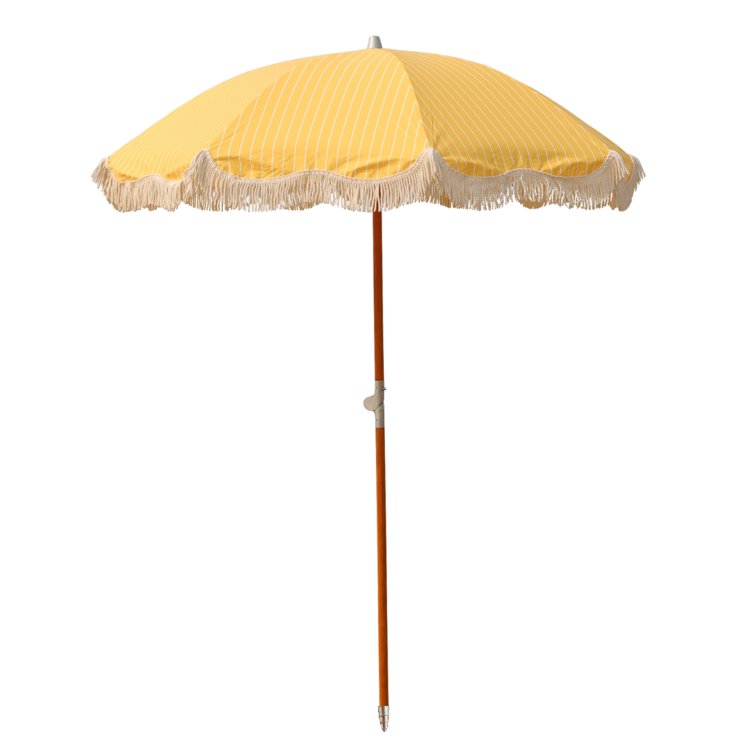 A beautiful wood poled beach umbrella with a yellow and white striped canopy and tassels on the edge.